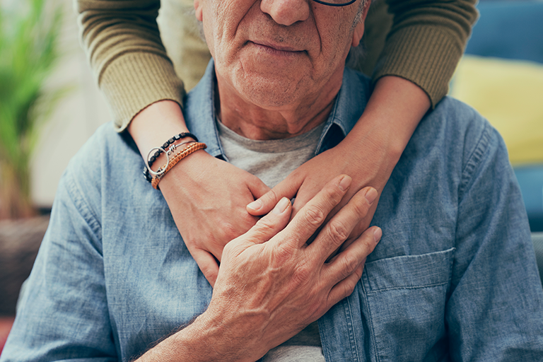 Image of an older man sitting with a caregiver hugging him